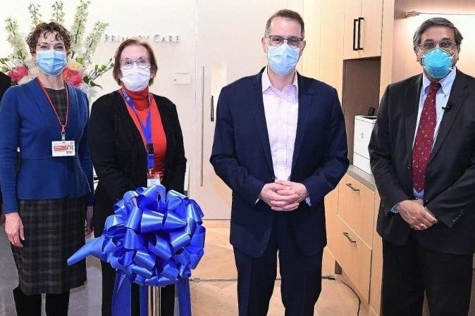 Four people stand in the Columbia Primary Care office waiting room with a big blue ribbon showing its grand opening