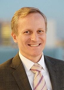 A headshot of David M. Greenberg who has blonde hair and is wearing a suit and tie.