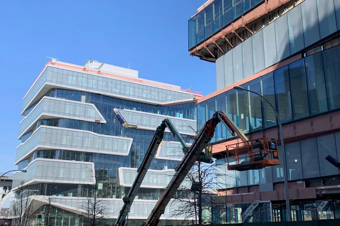 A worker on a crane inspects the facades of the new Columbia Business School Buildings