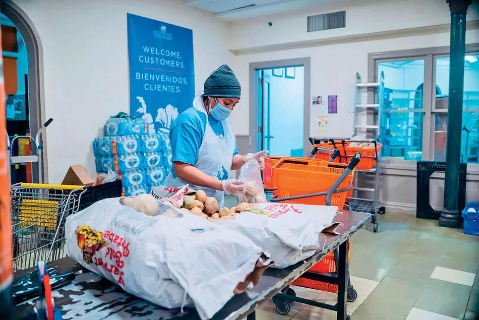 A food service employee is taking potatoes from a huge potato bag and putting it into a plastic bag inside of the prep kitchen