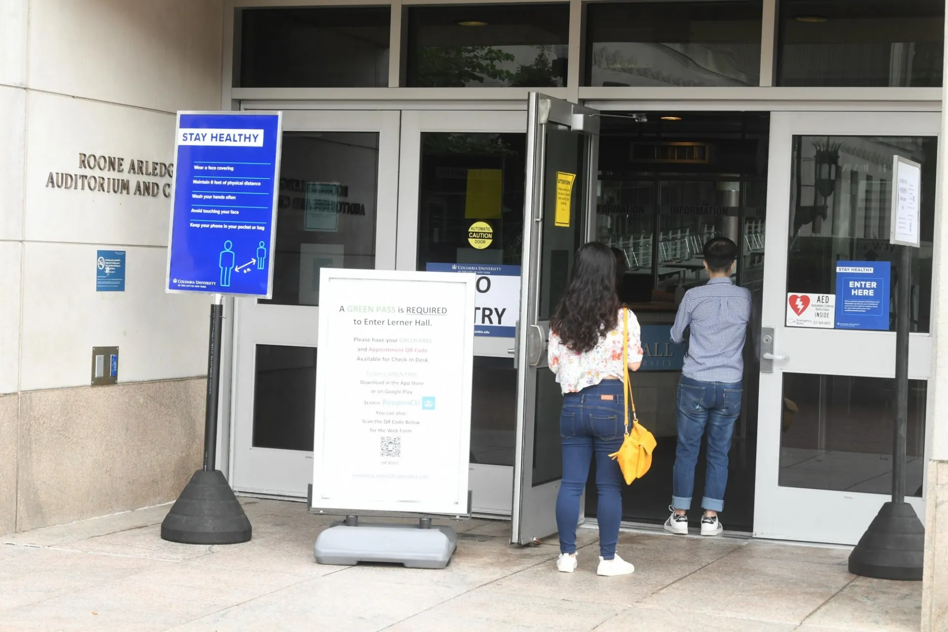 Students walk into Lerner Hall with COVID educational signage posted around the entrance doors.